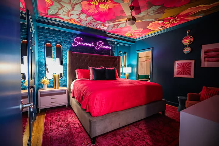 Amazing king size bed with premium pillows, bedding, a photo worthy neon sign that says "Savannah Stunners" and a sitting chair for your bestie to sit in! 
