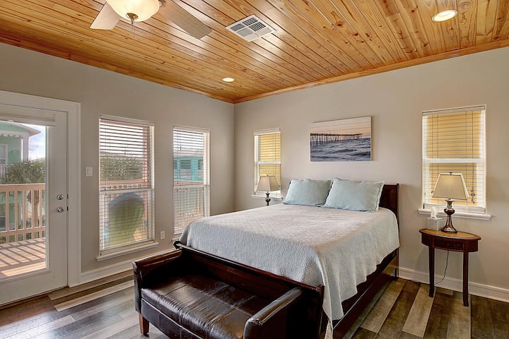 Relax under beautiful wood ceilings in your serene bedroom, featuring a comfortable bed and peaceful balcony access for morning coffee.