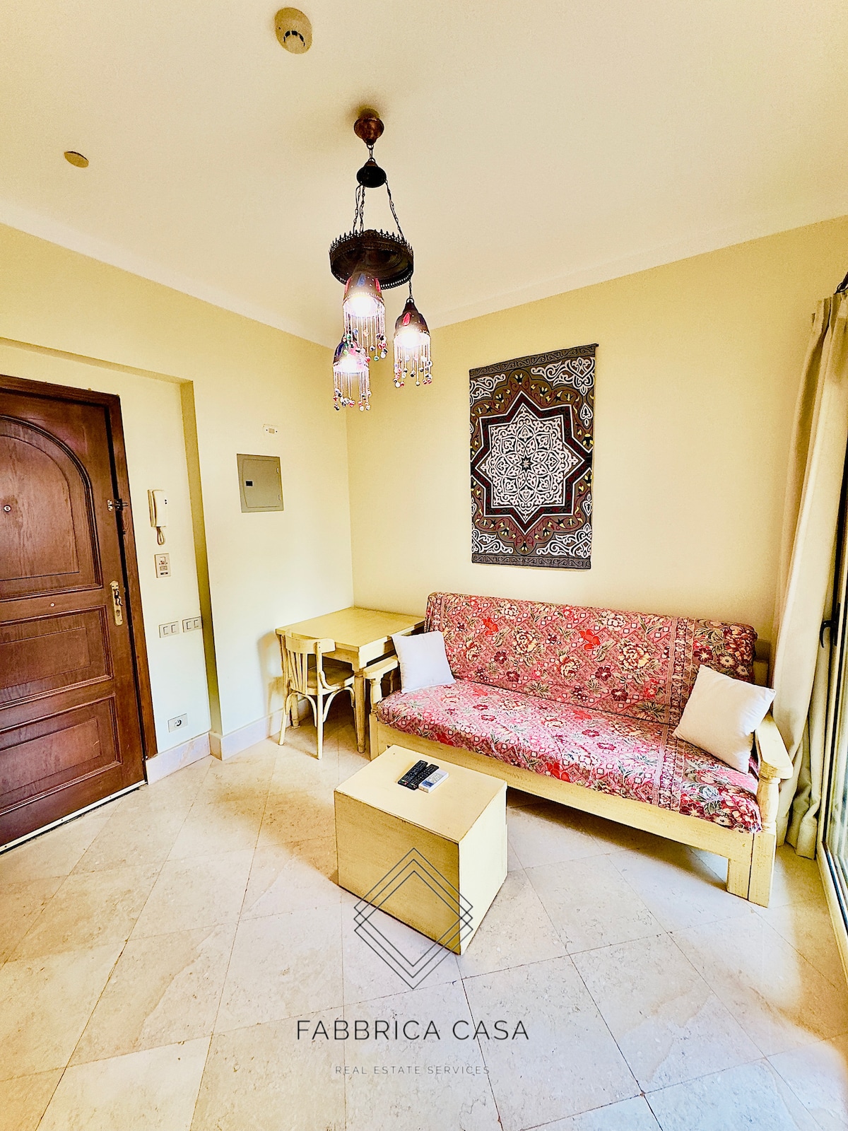 A cozy seating area features a patterned couch with cushion accents, complemented by a small wooden table and chairs. A decorative wall art piece enhances the space, while a stylish pendant lamp hangs from the ceiling, providing ambient light.