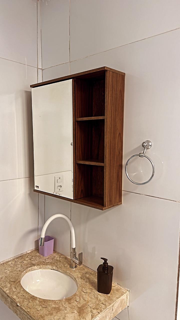 A modern bathroom features a compact cabinet with a mirrored door and open shelves for storage. A sleek sink is mounted on a light-colored countertop, complemented by a contemporary faucet. A towel ring is mounted on the wall next to the sink, providing functionality.