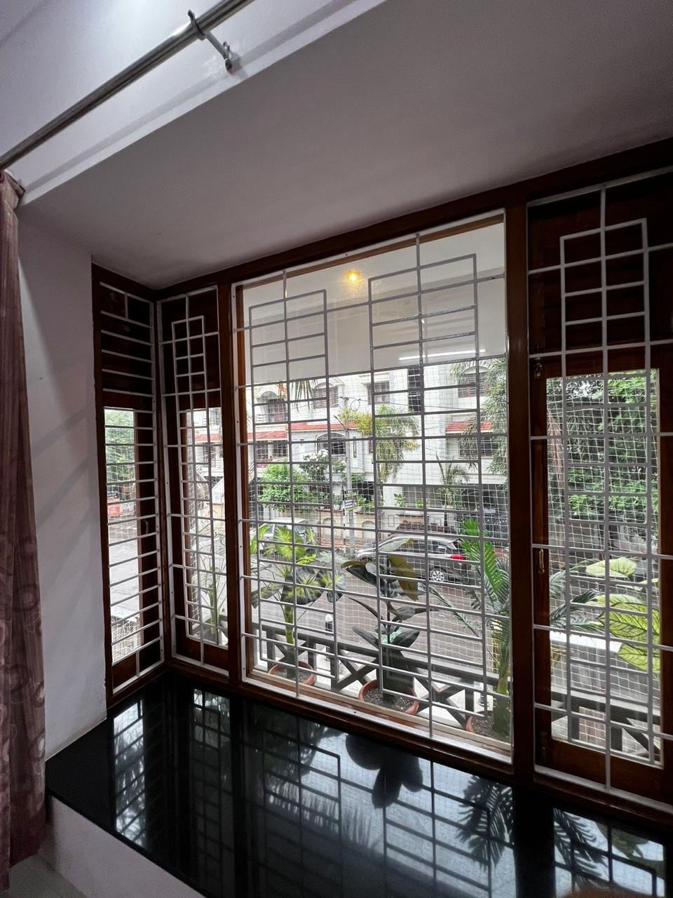 A wide window is framed with wooden accents and a decorative grid. Natural light fills the space, highlighting the black windowsill and offering a view of greenery and the surrounding area.