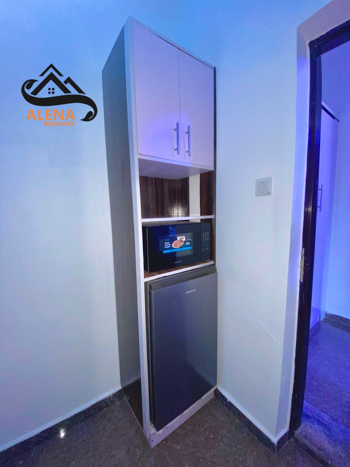 A sleek kitchen unit is showcased, featuring a compact refrigerator at the bottom and a microwave above. The cabinetry is finished in light colors, with an illuminated area highlighting the appliances, creating a clean and functional space.
