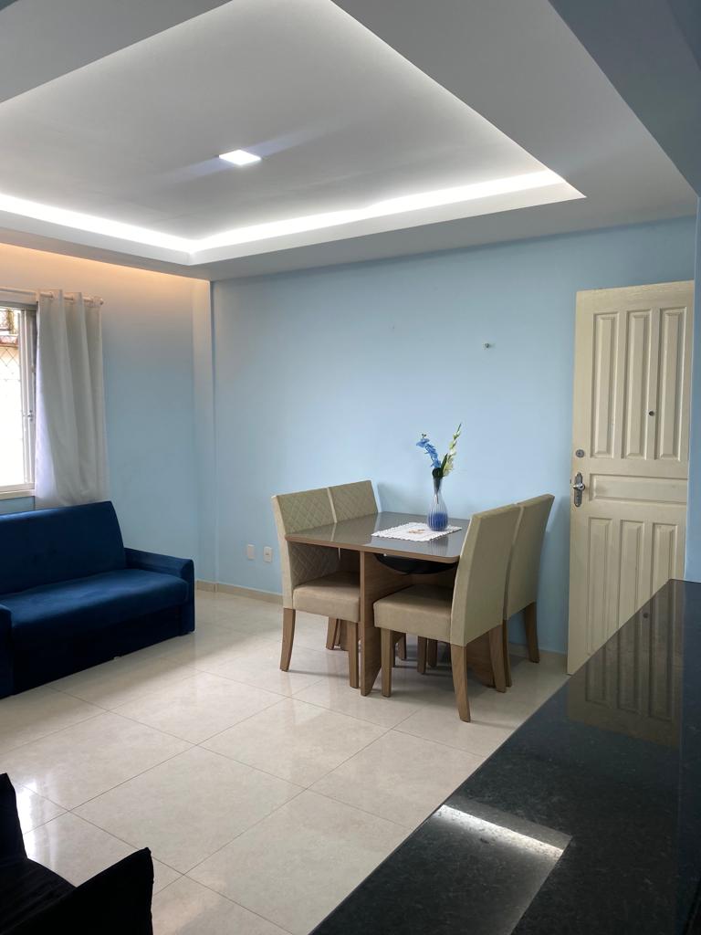 A light blue living space features a small dining area with a table and four chairs. A blue sofa is situated nearby. Natural light enters through a window adorned with sheer curtains. The door leading outside is visible, enhancing the room's accessibility.