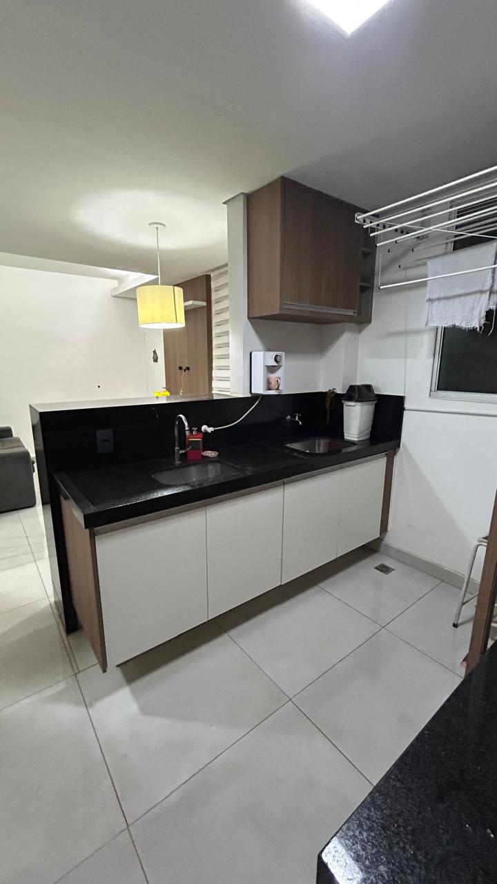 A modern kitchen features a granite countertop with a sink and faucets. Storage cabinets are situated below, and wall-mounted shelving is present for additional organization. A nearby window allows natural light in, while a pendant light hangs above, illuminating the space.