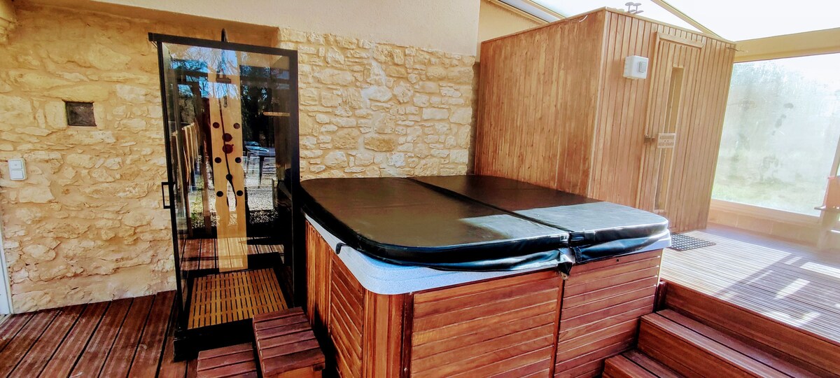 A spa area is visible, featuring a wooden enclosure surrounding a spa tub. The tub is fitted with a dark cover, and the wooden decking provides an inviting surface. A corner features a glass door leading to an outdoor space, allowing for natural light.