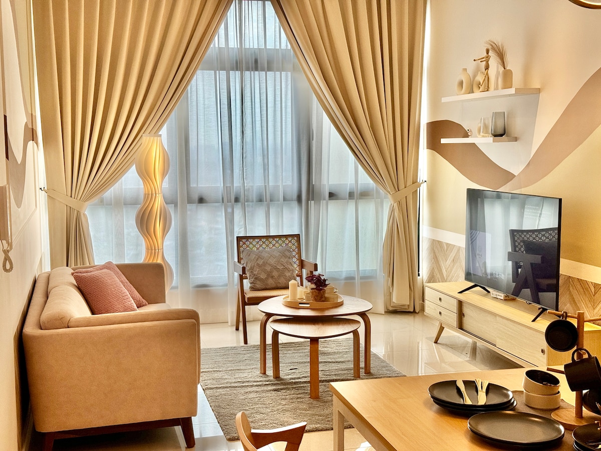 A well-lit living area is presented with large windows draped in flowing curtains. A soft-colored sofa faces a sleek television on a light wood media console. A round coffee table sits in the center, accompanied by two stylish chairs, creating an inviting space for relaxation.