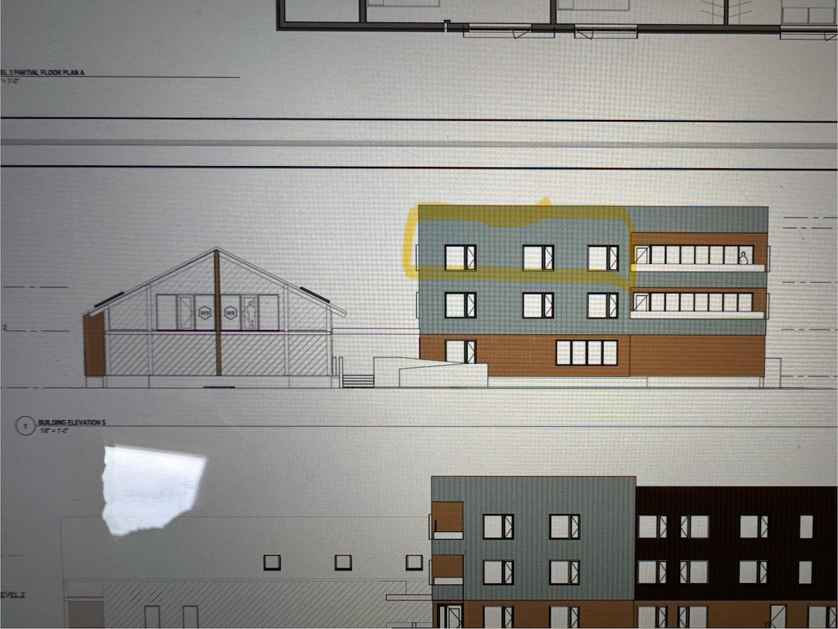 The architectural drawing presents a side elevation view of a two-story building featuring a mix of window designs and horizontal banding. The structure is complemented by a nearby lower building with a gable roof and multiple circular windows, enhancing the overall layout.
