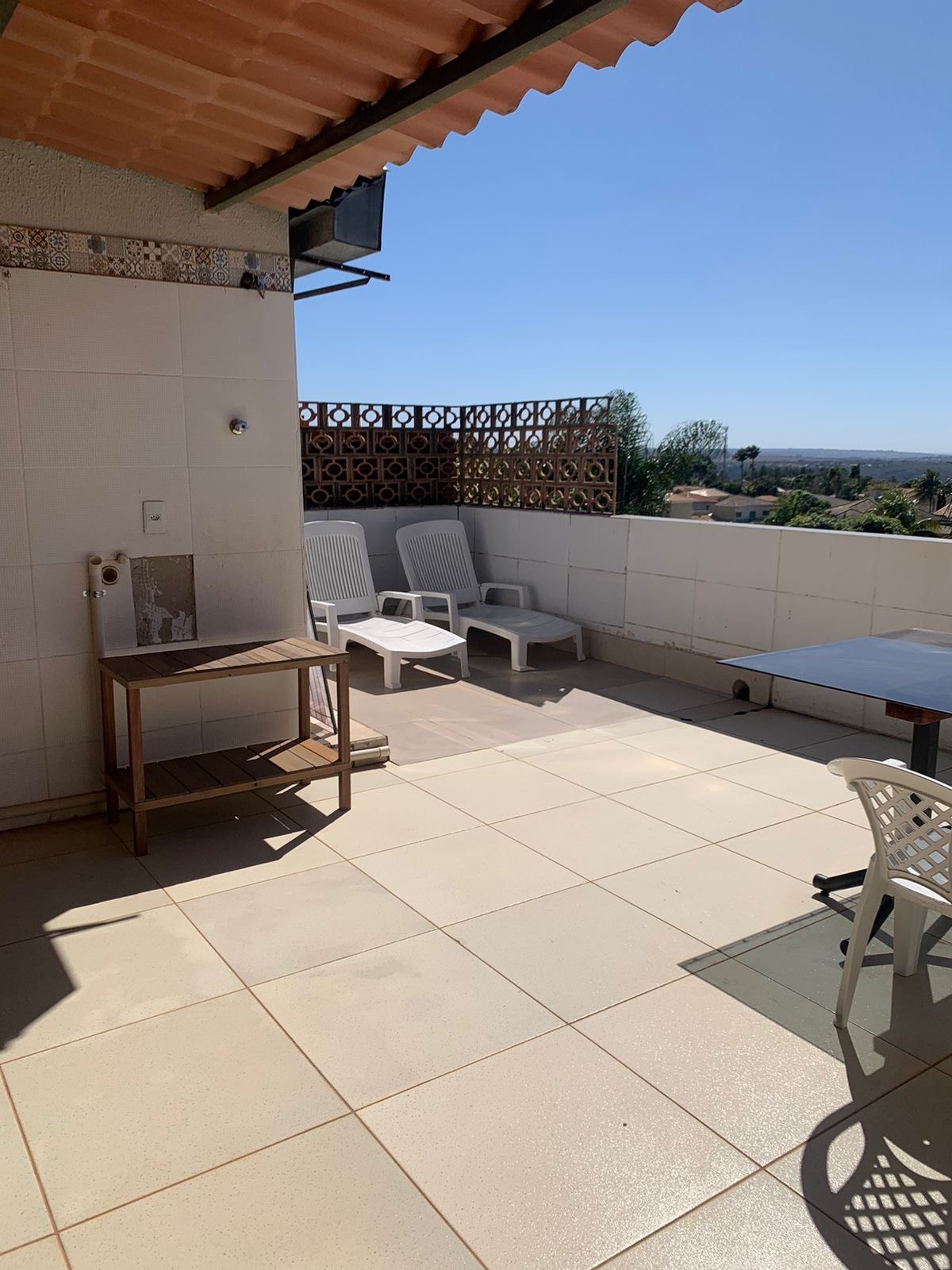 A private terrace is displayed, featuring a table and several simple lounge chairs, positioned under clear blue skies. Decorative privacy screens are visible, adding character to the outdoor space, which offers a view of the surrounding nature.