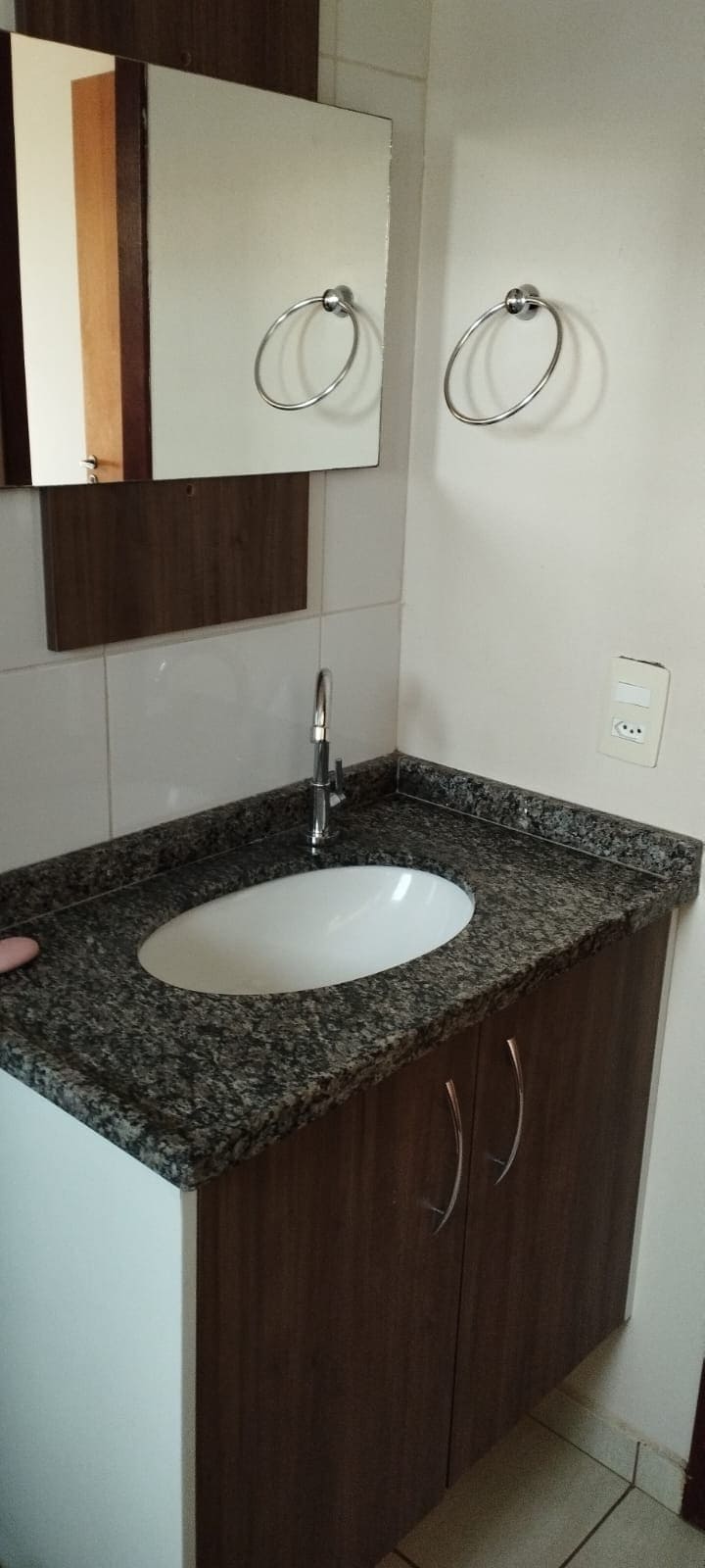 A compact bathroom area is showcased, featuring a sleek granite countertop with a round sink. A wall-mounted mirror enhances the space, while two towel holders are positioned nearby. The cabinetry combines wood finishes, contributing to a modern aesthetic.