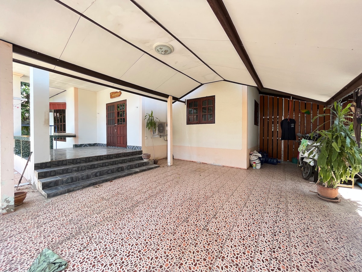 A covered entryway features a patterned stone floor, leading to a set of wooden double doors. A bike is parked alongside neatly stacked items. Potted plants add a touch of greenery, while ample natural light filters through large windows.