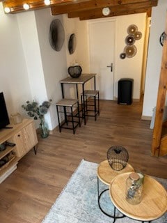 An inviting living area features a light wooden floor with a comfortable seating arrangement, including two round coffee tables. A television unit with decorative elements is placed nearby. Wall art and decorative fans add character, while the entrance to the space leads to additional rooms.