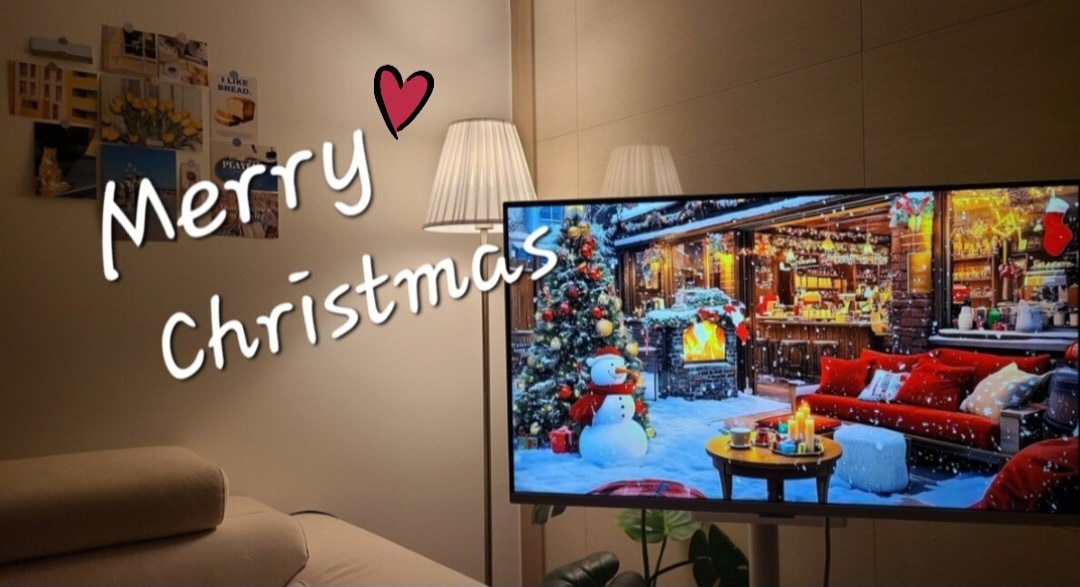 A modern living area features a large television displaying a festive winter scene with a decorated tree and a snowman. Soft light is cast by nearby lamps against neutral-toned walls, creating a cozy ambiance.