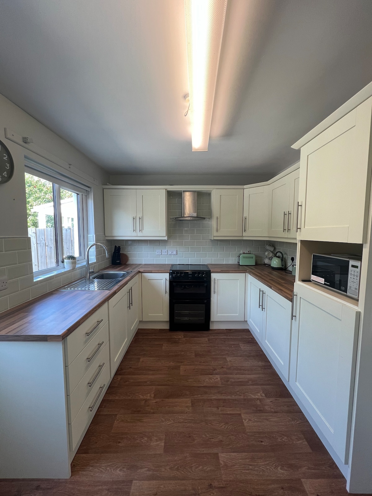 The kitchen features modern cabinetry with a light finish and wooden countertops. A gas stove and a microwave are positioned for convenience. Ample natural light streams in through the large window, illuminating the space. A clean, minimalist design enhances the overall functionality.
