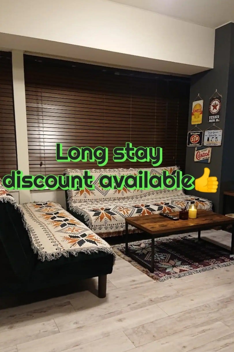 The living area features two sofa beds with decorative throws, complemented by a wooden coffee table. Natural light filters through wooden blinds, creating a warm ambiance. Decor items and wall art add character to the space.