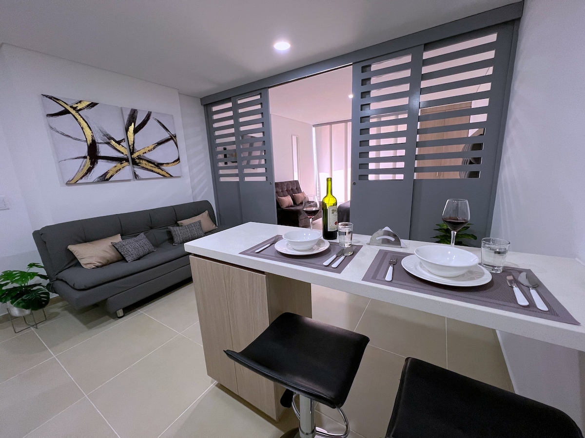 A modern dining area is featured with a sleek table set for two. A cozy sofa is positioned nearby, complemented by decorative cushions. Light pours in through the partially open sliding doors, illuminating the space with a fresh ambiance.