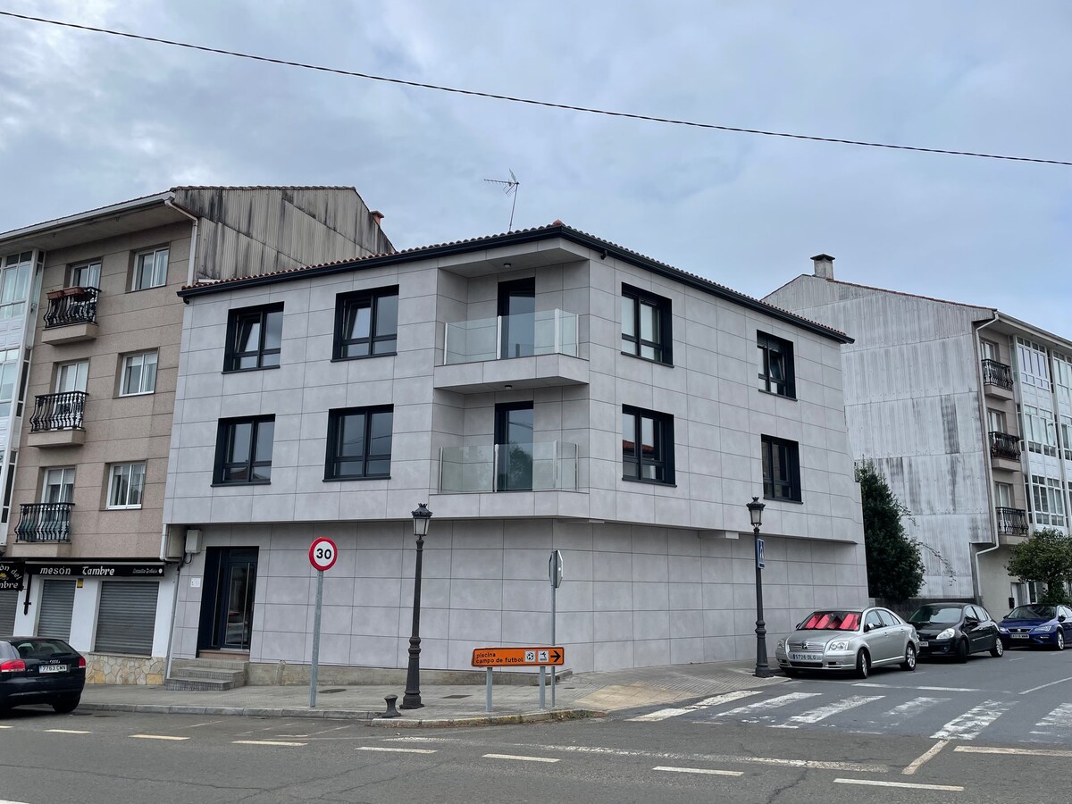 The modern three-story building features a sleek facade with large windows and a glass balcony on the second floor. Its corner location allows for ample natural light, and a clean, minimalist design is emphasized by the neutral color palette. Surrounding streets and nearby buildings are visible.