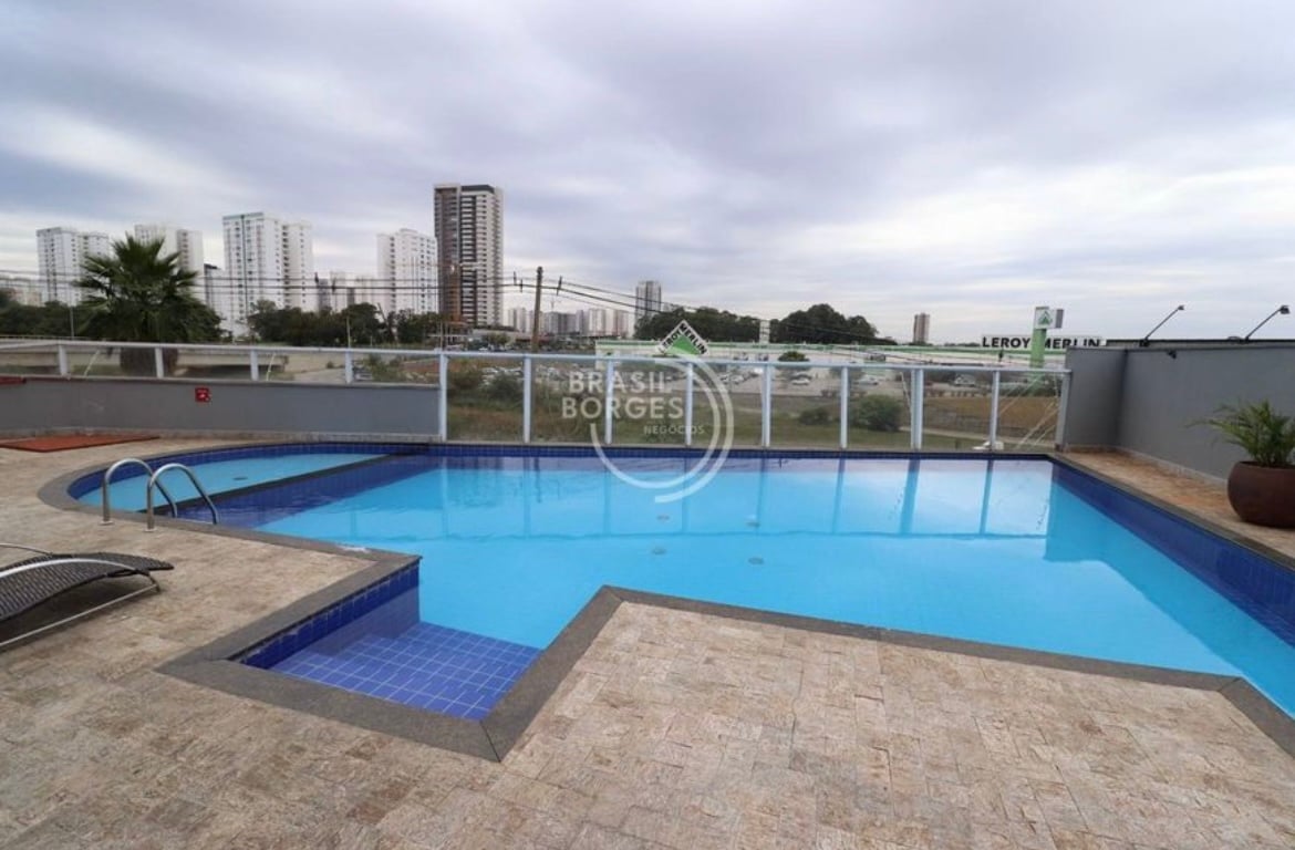 A large swimming pool is framed by a stone terrace, featuring steps leading into the clear water. Surrounding the pool, a glass railing provides unobstructed views of the skyline, while lounge chairs are placed nearby for relaxation.