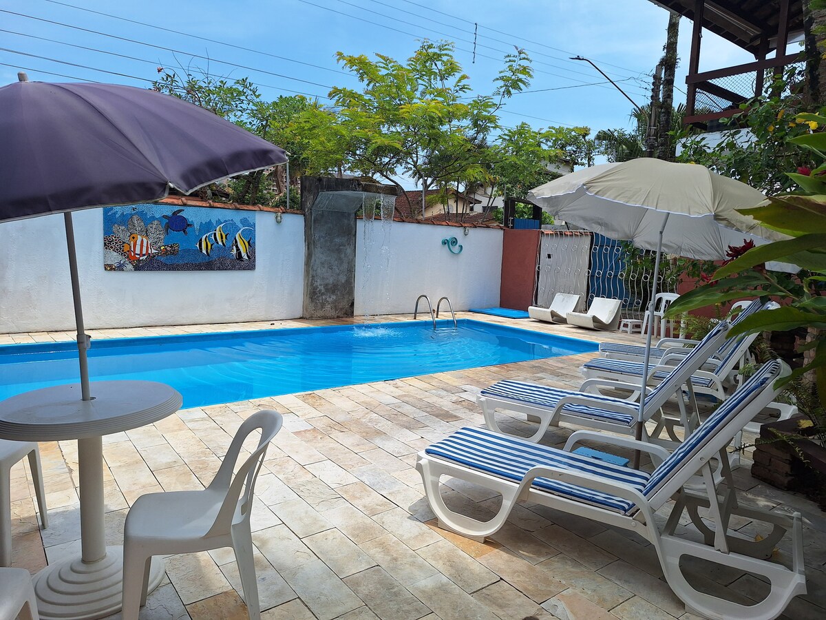 The outdoor pool area features a clear blue pool surrounded by sun loungers and umbrellas. A colorful mural depicting marine life is painted on the wall, adding visual interest. The space is framed by green foliage, creating a tranquil atmosphere.