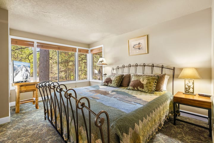 Un dormitorio principal tranquilo y acogedor cuenta con una cómoda cama king y grandes ventanales con hermosas vistas al bosque.