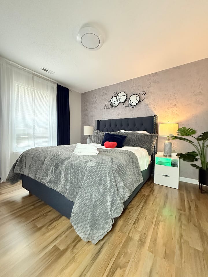  غرفة نوم مريحة للضيوف – سرير مريح مع مفارش رمادية أنيقة وديكور عصري.