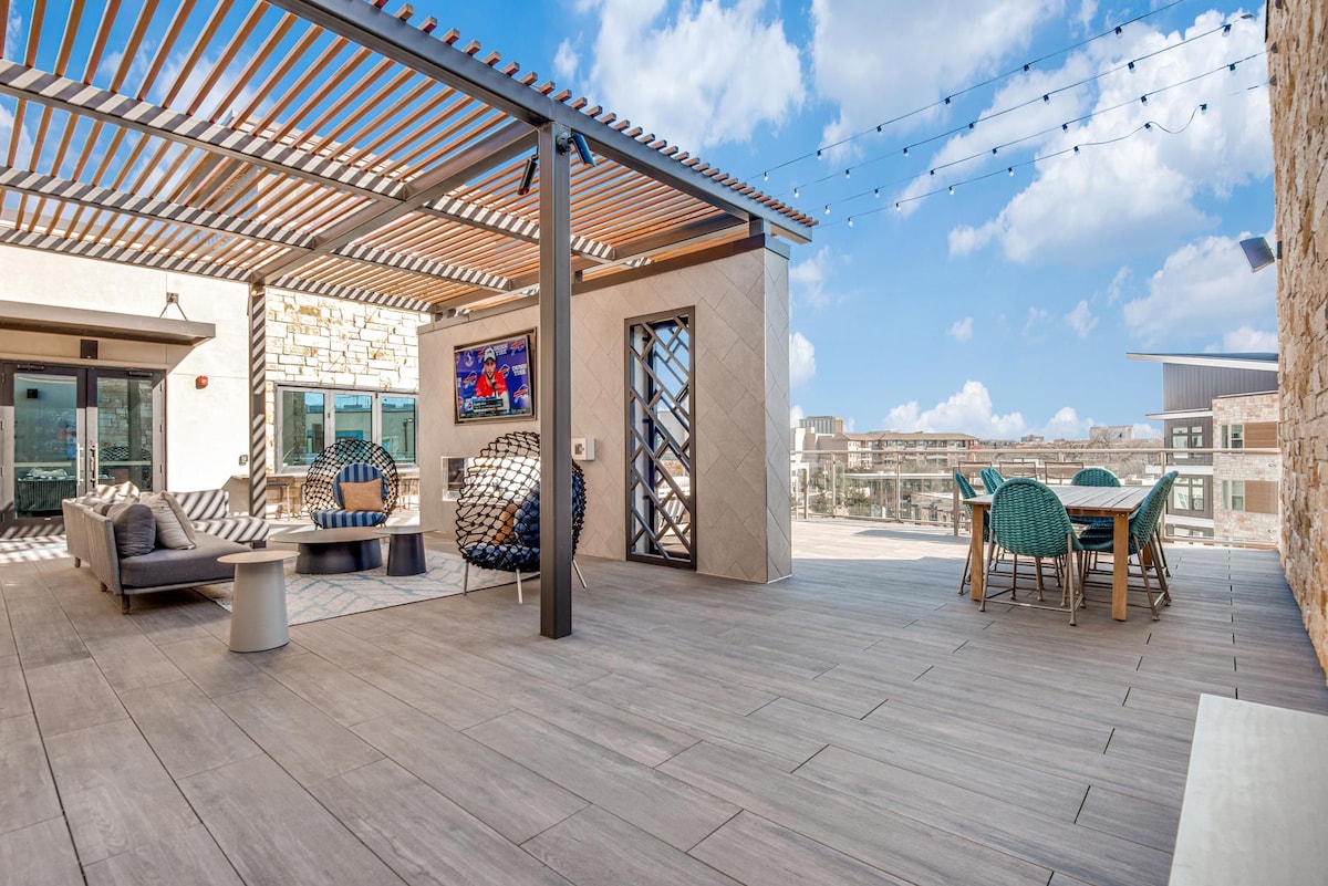 An outdoor terrace offers ample seating with a modern couch, playful accent chairs, and a dining table. String lights create a warm ambiance, while large windows enhance views of the surrounding area. The design features a mix of natural materials and contemporary finishes.