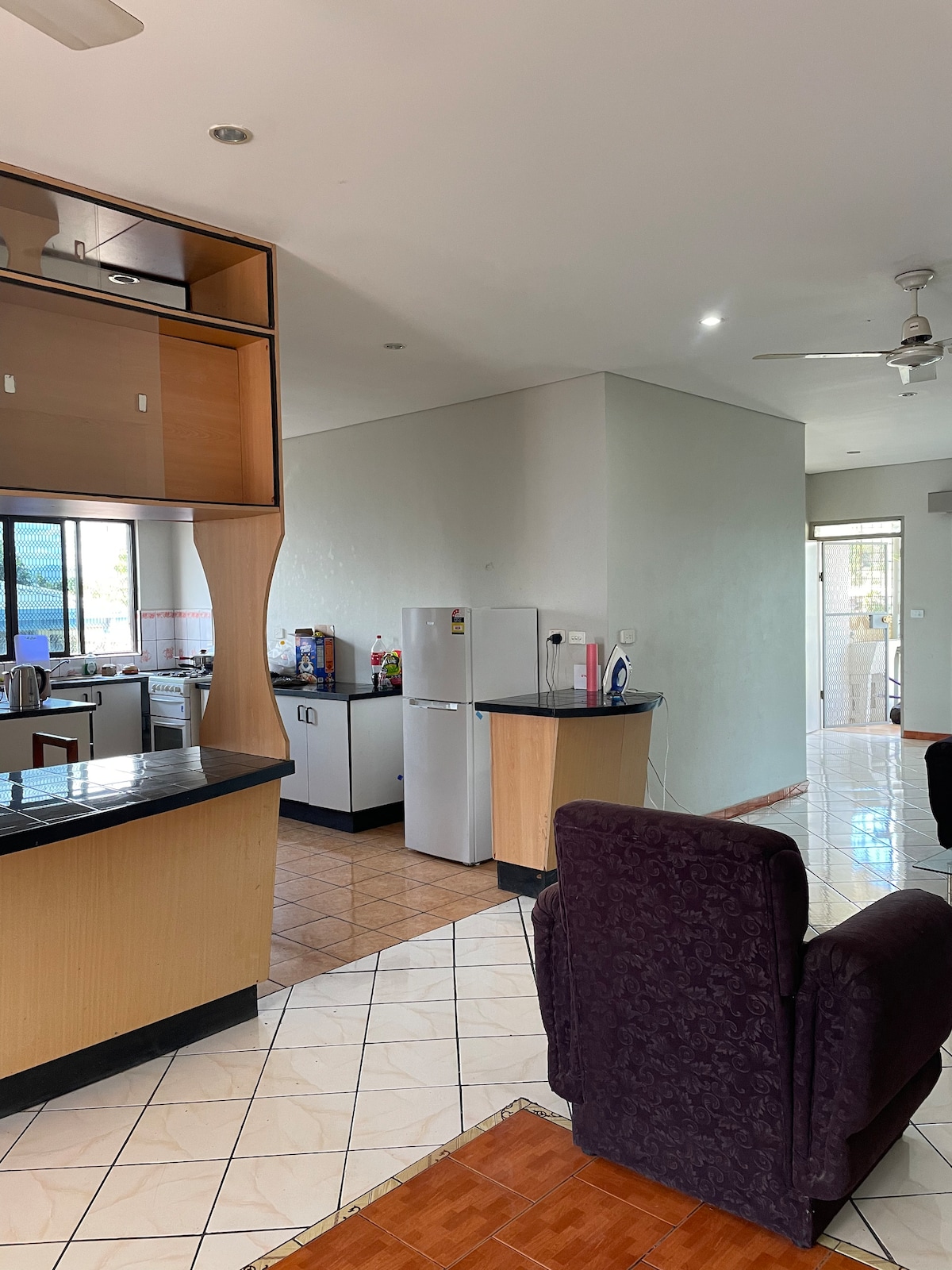 The open kitchen features modern appliances and ample counter space. A dining area is visible, complemented by a seating area with a couple of chairs. Natural light flows in from the windows, enhancing the spaciousness of the living area.
