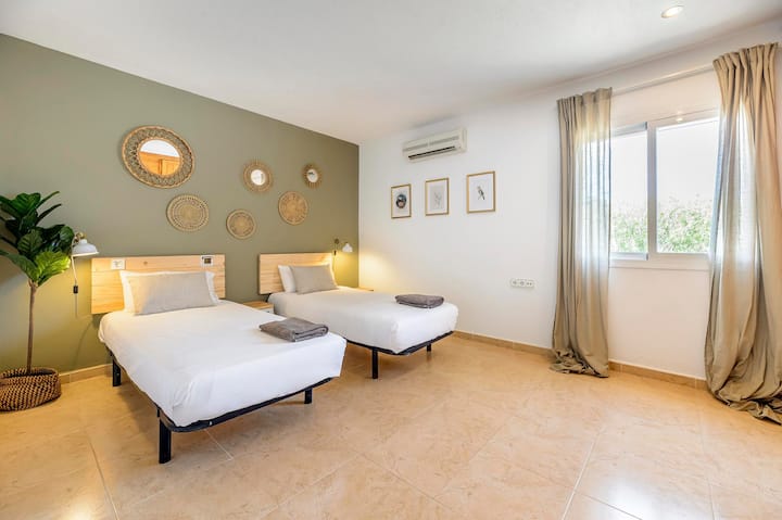 Twin bedroom with green feature wall and rattan mirror display, Villa Suki, Ibiza.