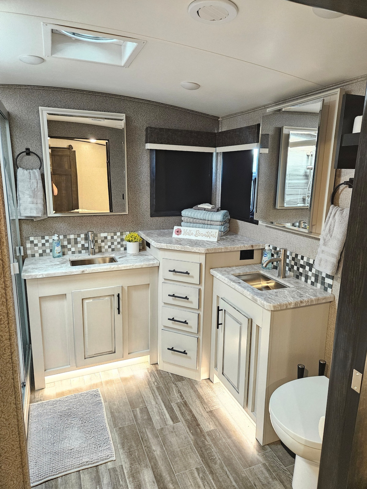 A well-appointed bathroom features a spacious layout with dual vanities and ample storage. A walk-in shower with built-in seating is present, along with a modern toilet. Natural light is provided through a skylight, and decorative elements add a touch of style.