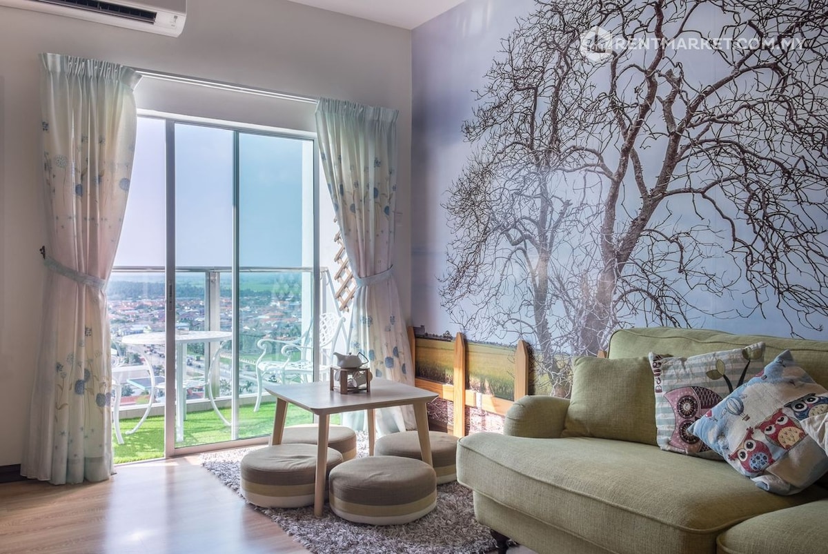 A cozy living area features a light green sofa adorned with decorative pillows. Large windows allow natural light to fill the space, offering views of the surroundings. A light-colored coffee table sits in front, complemented by soft curtains with a floral pattern.