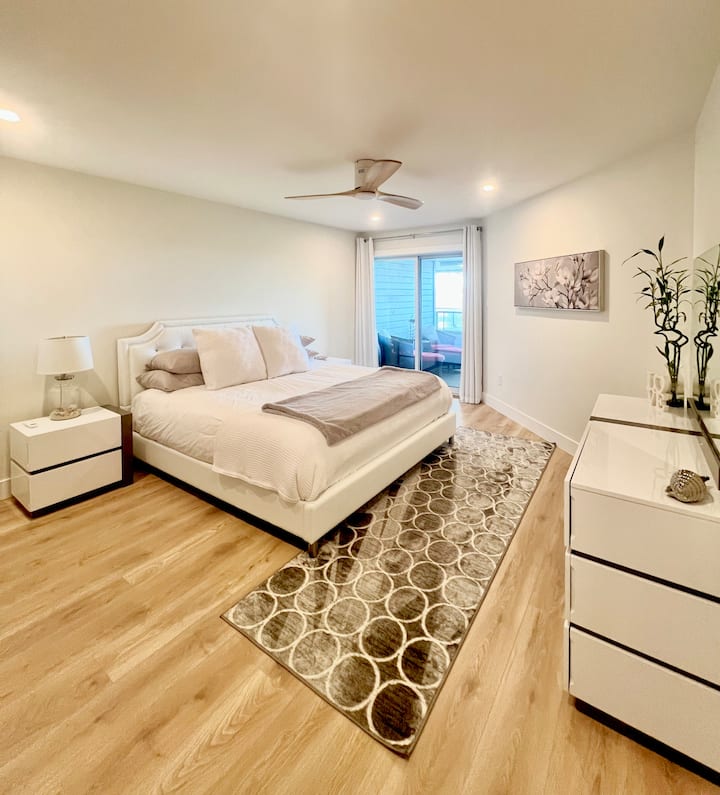 غرفة نوم رئيسية مع سرير بحجم كينج وخزانة ملابس وخزائن ومدفأة وشرفة خاصة مواجهة للمحيط.