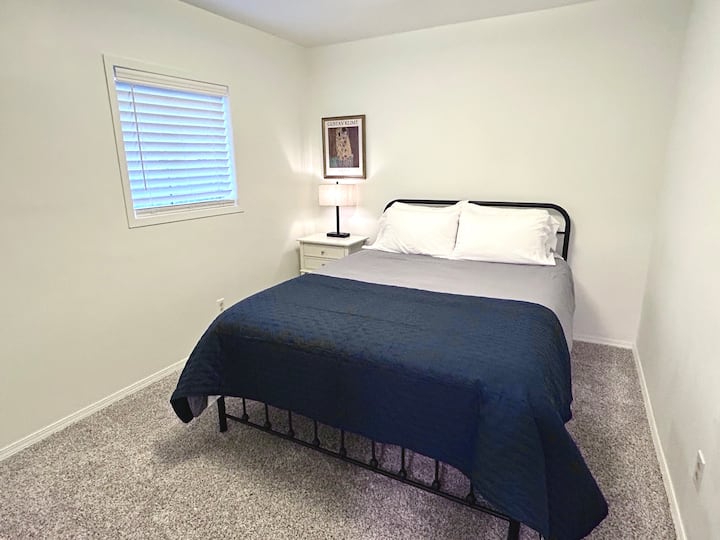 The second bedroom on the main floor includes a queen-sized bed, dresser, nightstand with lamp, and a closet for hanging clothes — a comfortable, well-appointed space for a restful night’s sleep.