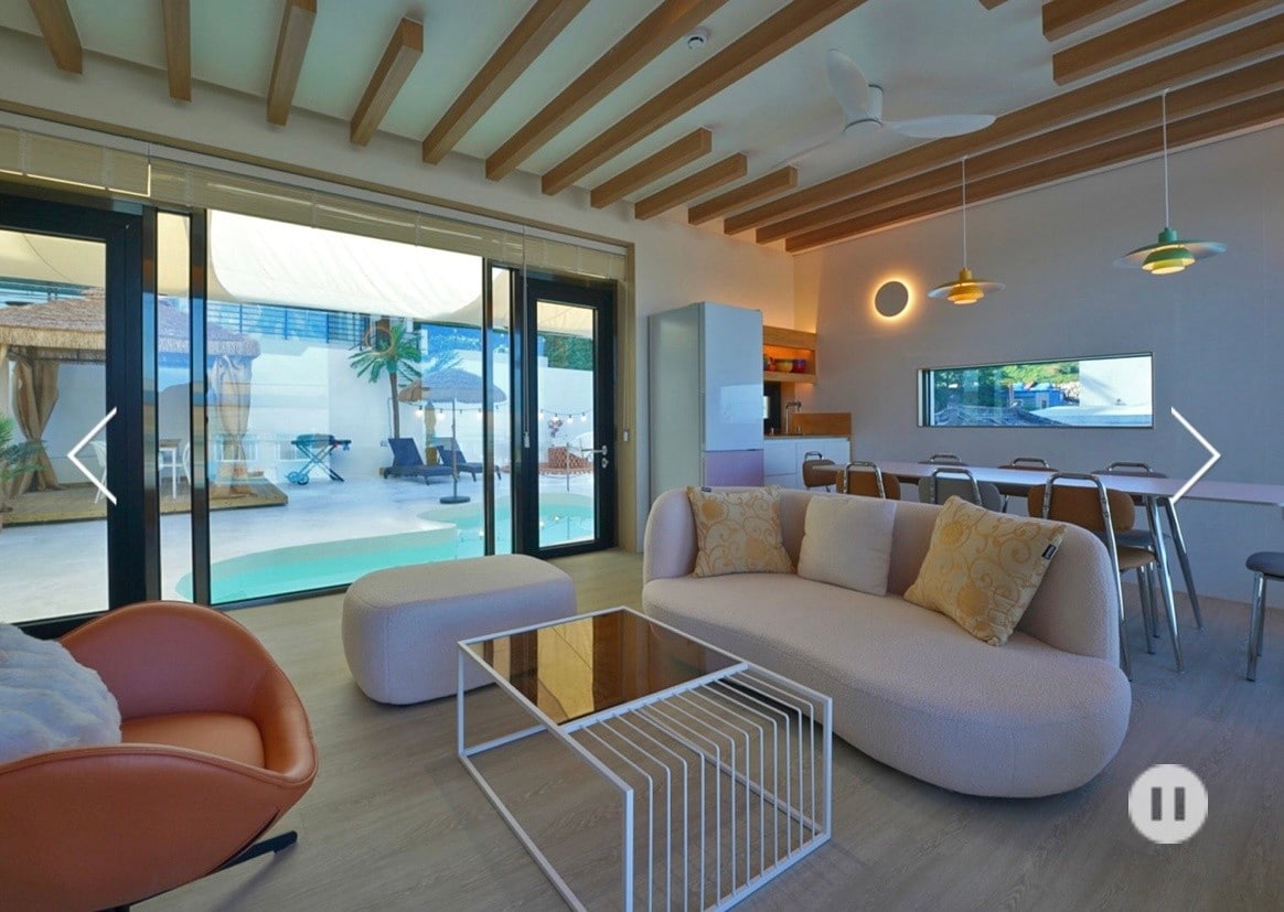 An open living area is showcased, featuring a modern sofa and an accent chair. Large glass doors provide a view of the outdoor space with a pool. A dining table with metal chairs complements a minimalistic design, while recessed lighting adds subtle illumination.