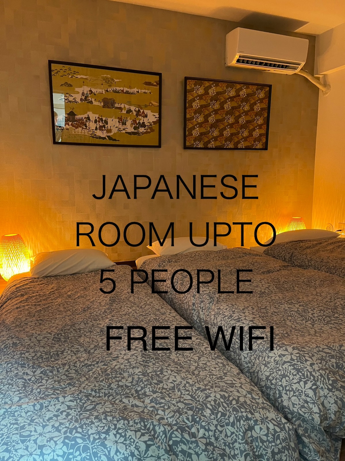 A Japanese-style room is presented with three single mattresses arranged on a textured floor. Soft lighting from bedside lamps casts a warm glow, enhancing the calming environment. Two art pieces adorn the walls, adding cultural elements to the space designed for up to five guests.