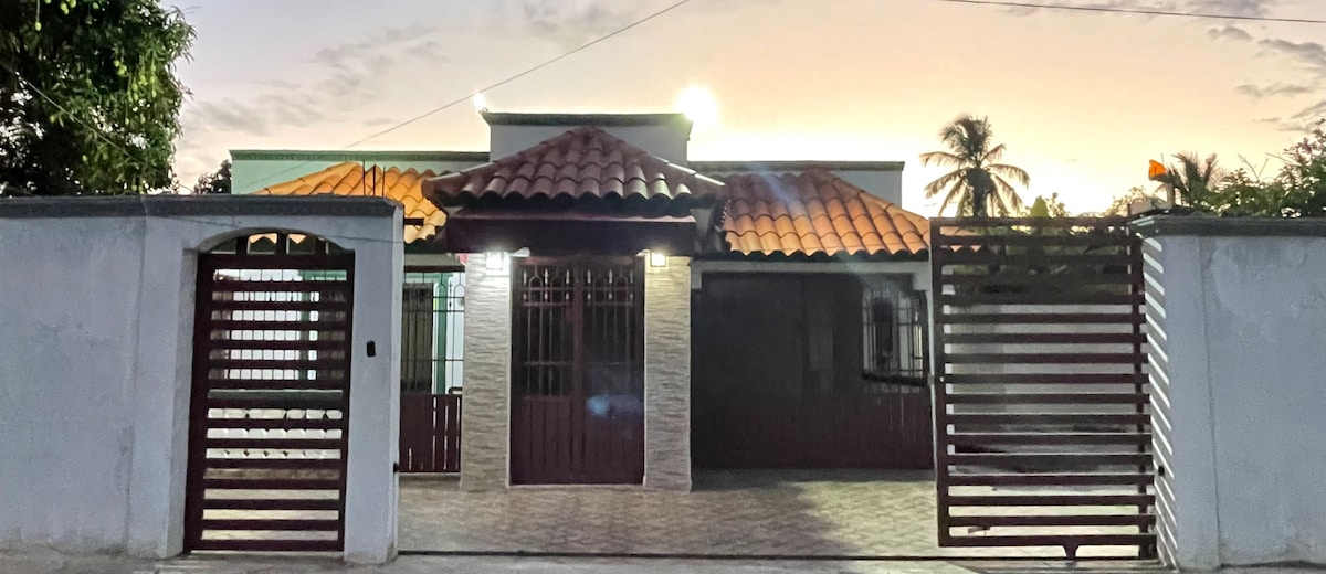 A charming house exterior features a tiled roof and a gated entrance. The facade displays a combination of stone and wooden elements. Surrounding trees contribute to a natural atmosphere, while the evening light enhances the overall appeal of the property.