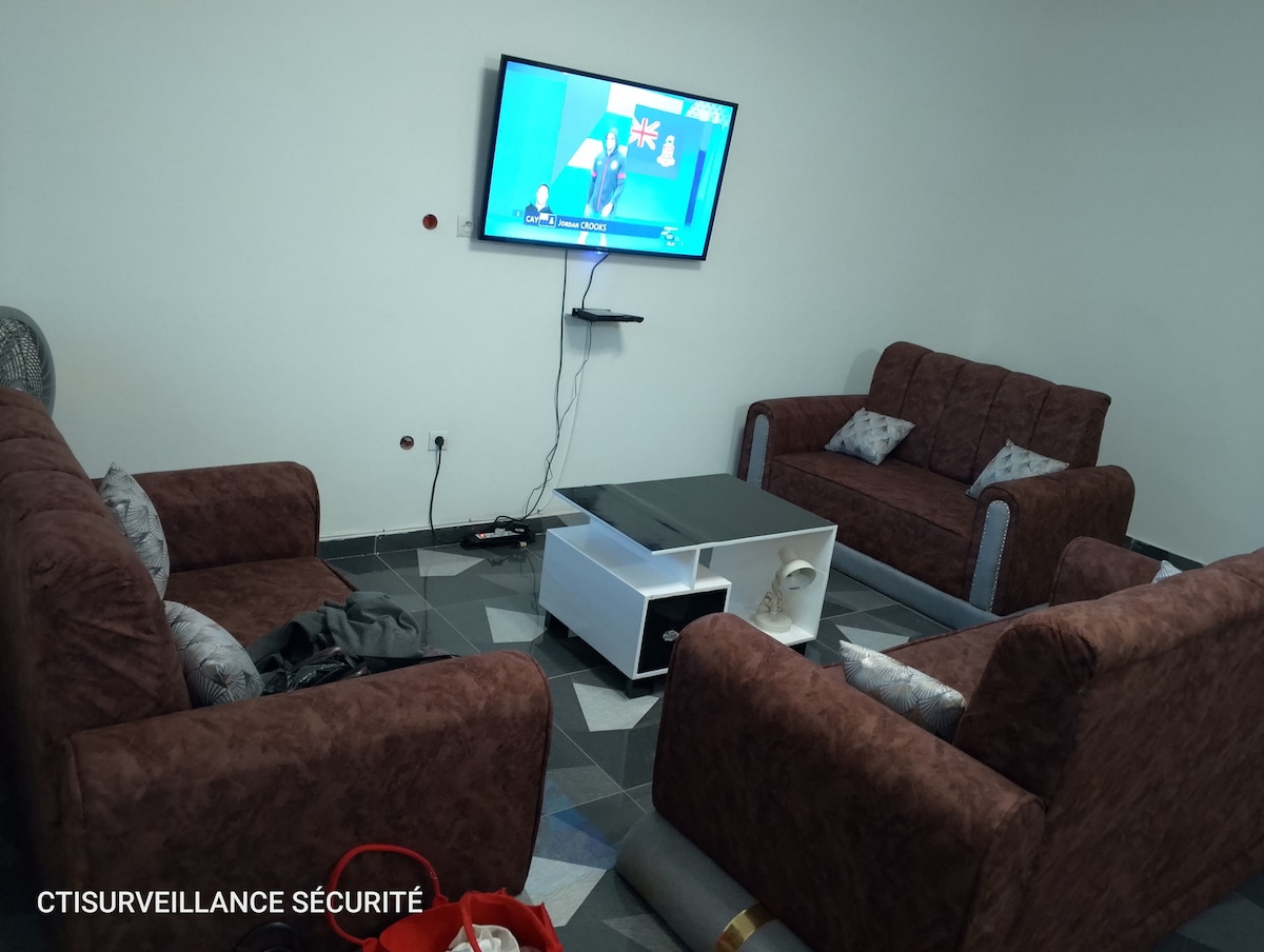A comfortable seating area is furnished with two brown sofas and a central coffee table. A television is mounted on the wall, providing entertainment options, while the floor features a stylish black and white tile pattern.