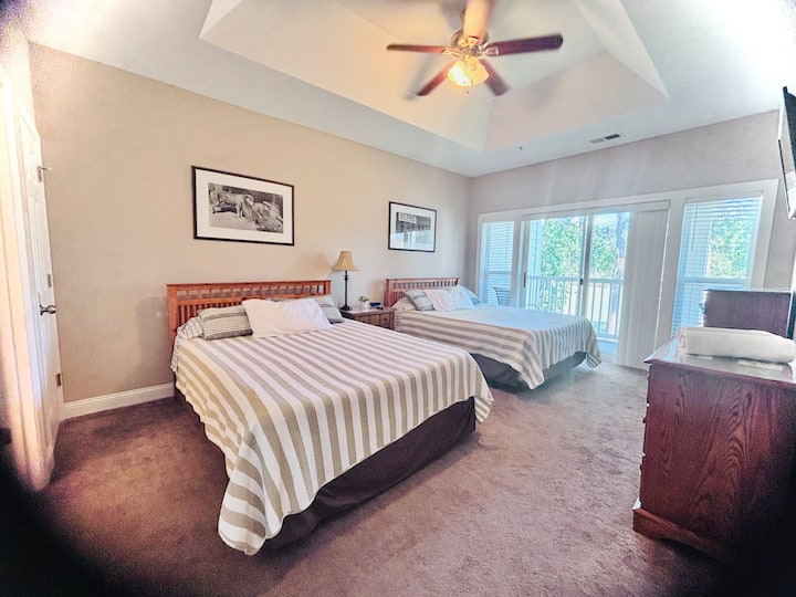 חדר שינה ראשי גדול עם מאוורר תקרה, חדר רחצה ראשי צמוד, ודלת הזזה גדולה המובילה למרפסת עם נופים מדהימים של שקיעות מערביות מעל מסלולי הגולף של World Tour Golf Links