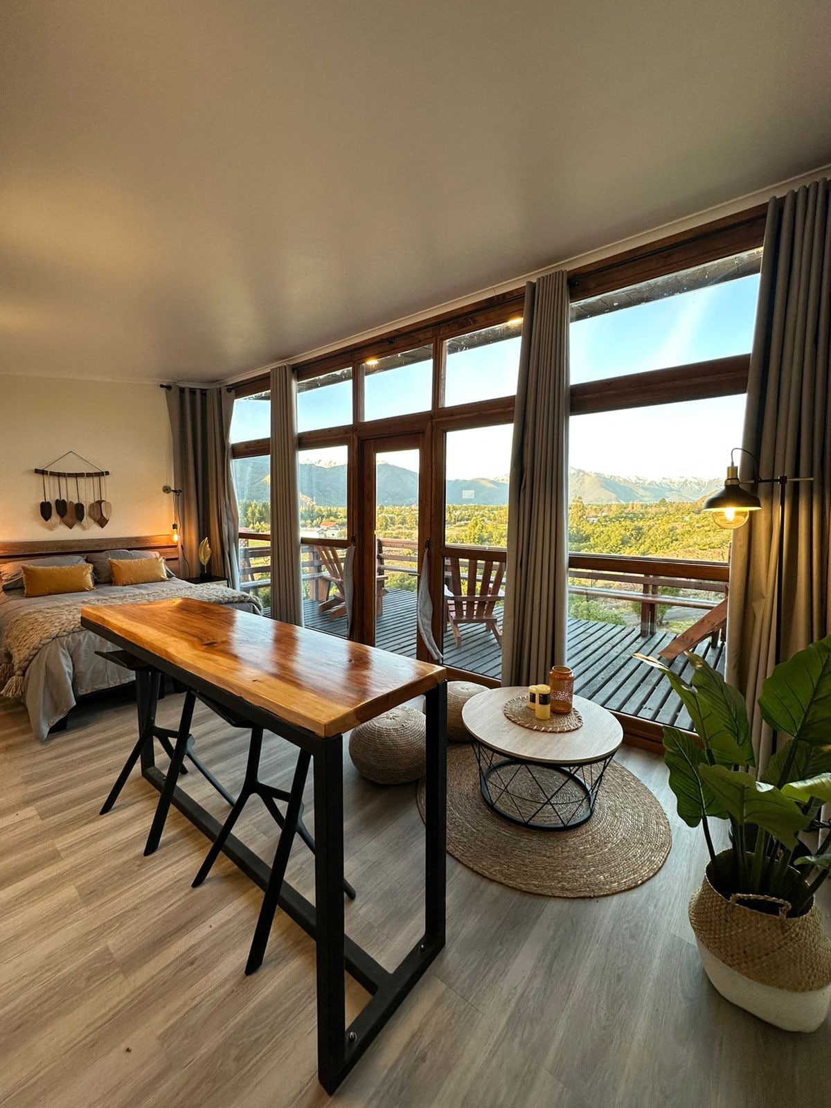 The spacious interior features large windows offering panoramic views of the surrounding nature. A wooden dining table stands in the center, accompanied by cozy seating. Soft lighting enhances the relaxing atmosphere, while a plant adds a touch of greenery to the inviting space.