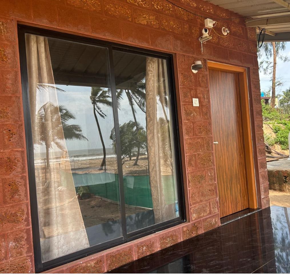 A door leads to an entrance area featuring large glass windows, providing a view of the palm trees and the beach beyond. Light, flowing curtains are positioned at the sides of the window, complementing the warm-hued brick exterior.