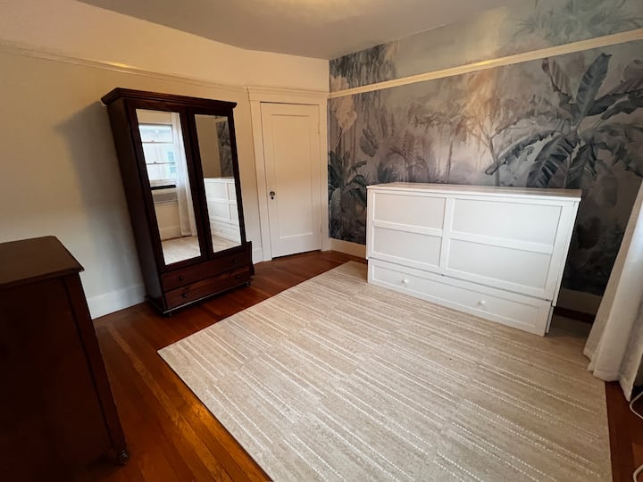 חדר שינה עם מיטת קווין סייז של מרפי. וילונות האפלה ושקעים מעל חלונות. כיסוי הרצפה הוא מזרן מרופד של בית נועה שמתאים לשימוש כאזור משחקים או חדר יוגה/אימון כשהמיטה מקופלת.