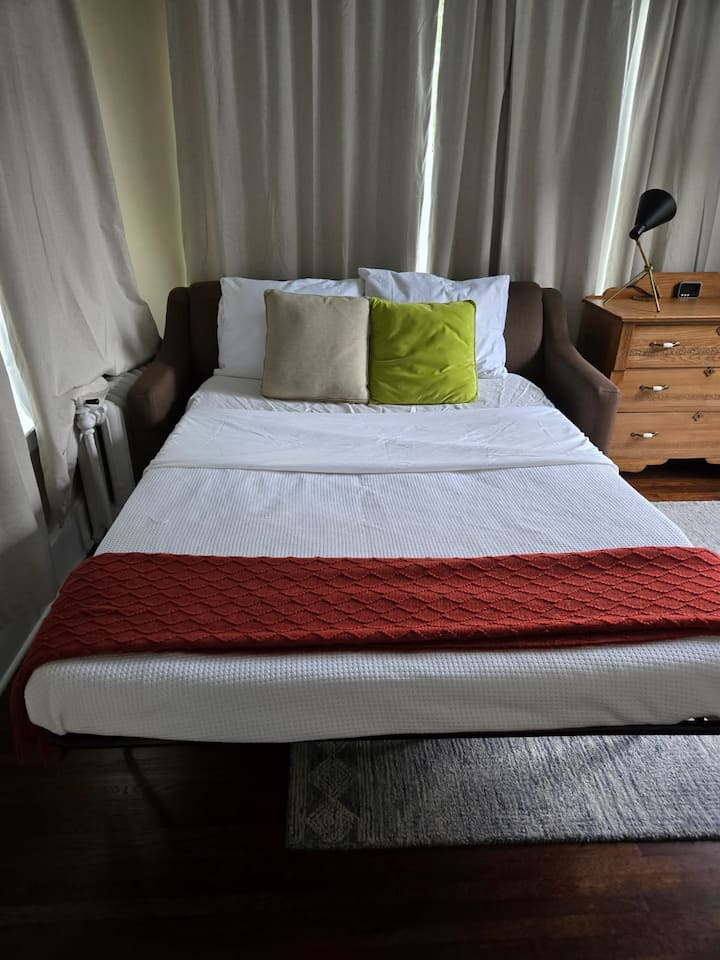 חדר גמיש. כיסא סיבובי, שולחן בנקאי, ספה נפתחת, וילונות להחשיכה מלאה.