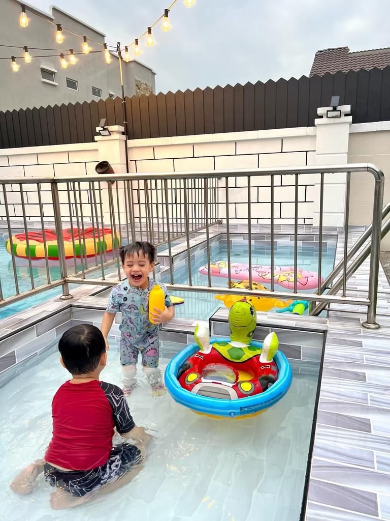 A private swimming pool area features a shallow section suitable for young children, with colorful inflatable toys visible. Two children are engaged in play, one standing and the other seated in a floating toy. Soft lighting adds a pleasant ambiance to the space.