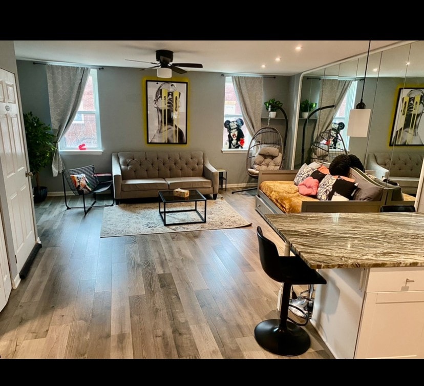 The open-plan living area features a comfy sofa adorned with colorful throw pillows and a stylish coffee table. Large windows allow ample natural light. A dining area with seating is positioned nearby, while a kitchen island provides additional space. A cozy accent chair adds a touch of comfort.