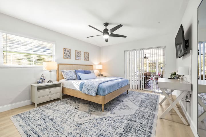 Bedroom 1 | Primary bedroom with King bed, dedicated workspace, smart TV, closet storage with hangers, hamper, luggage racks, ceiling fan, and access to screened-in lanai/pool.