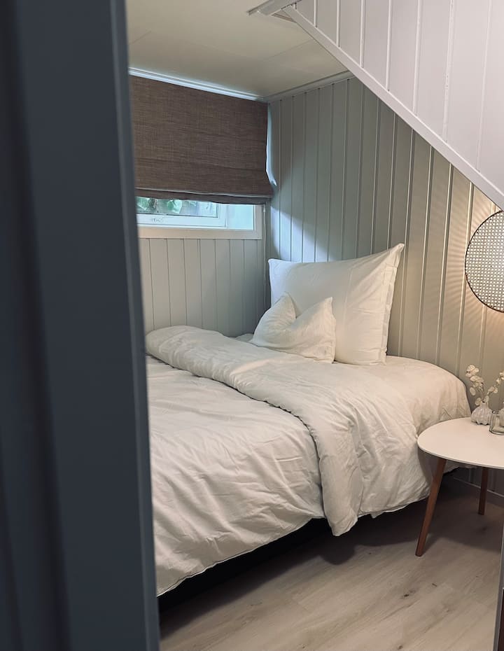 Soveværelse nedenunder med queensize-seng, læselys, tv med støbemuligheder, gulvvarme og tøjopbevaring i garderobeskabet. Her finder du også en kapselmaskine, hvis du vil nyde din morgenkaffe i sengen samt et udvalg af læsematerialer.