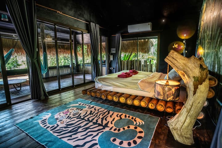 Chambre climatisée avec grandes fenêtres, vue sur la mer et décoration tropicale. Doté d'un lit en bambou confortable et d'un environnement paisible dans la jungle, offrant la retraite parfaite pour la détente et le confort.