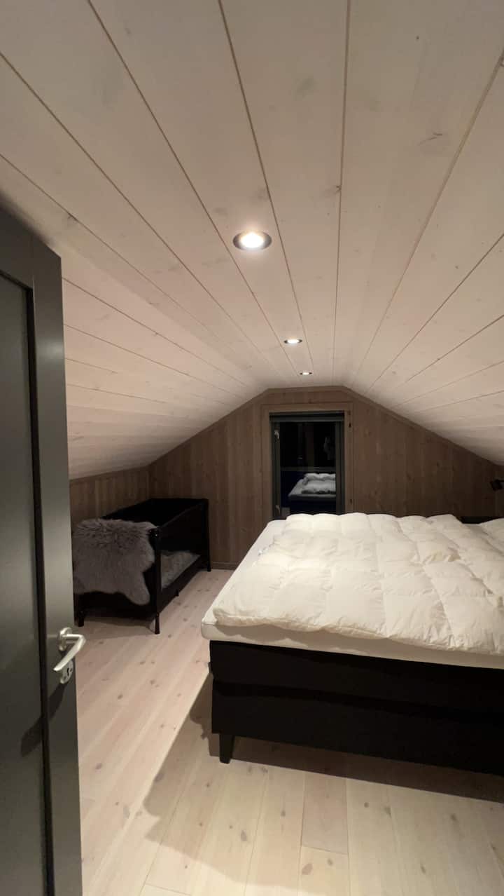 Lit 180x200 Signature Collection avec couettes en duvet Høie et oreillers Høie. Lit bébé avec matelas et couette. Tables de chevet murales et lampes murales en plus d'un endroit à intensité variable sur les plafonds 