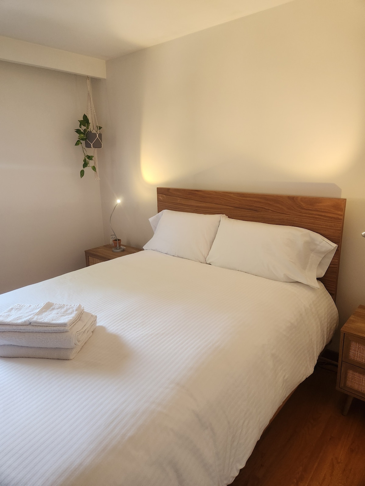 A private room features a spacious queen bed, accompanied by neatly arranged linens. Soft lighting from bedside lamps creates a serene ambiance, while wooden furniture complements the warm tones throughout the room.