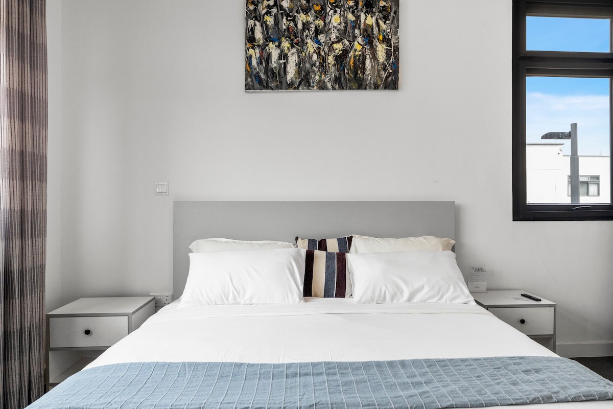 غرفة نوم رئيسية واسعة تتميز بسرير كينج وحمام داخلي وخزانة ملابس مدمجة. استمتع بتكييف الهواء وتلفزيون مثبت على الحائط وإضاءة طبيعية ساطعة من النوافذ الكبيرة. تخلق التشطيبات الحديثة جوًا هادئًا ومريحًا.