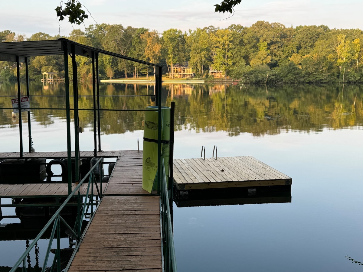 A private dock extends into the calm waters of Lake Catherine, featuring a wooden swim platform moored nearby. Lush greenery lines the opposite shore, reflecting softly in the water's surface, enhancing the serene atmosphere of the secluded retreat.