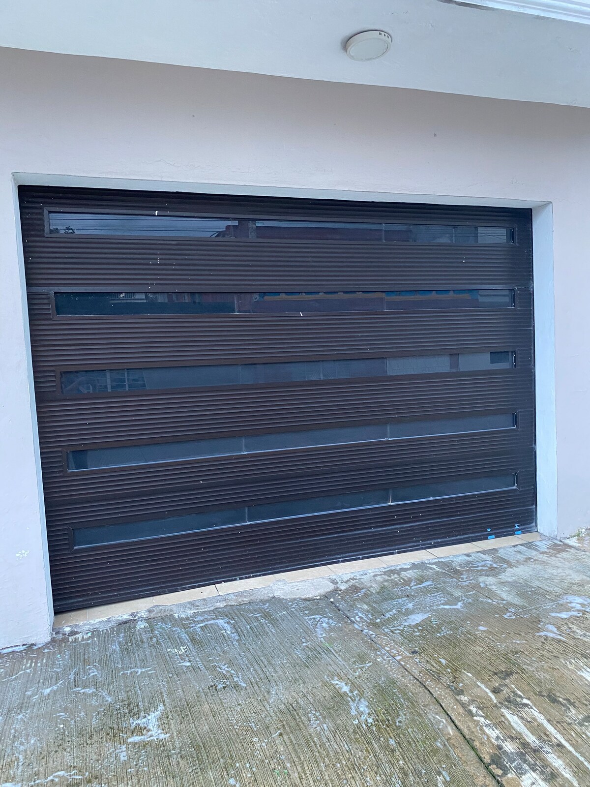 A modern garage door features horizontal slats with transparent windows, allowing glimpses of the interior. The door's design is both functional and contemporary, situated in front of a smooth concrete surface that leads up to the entrance.